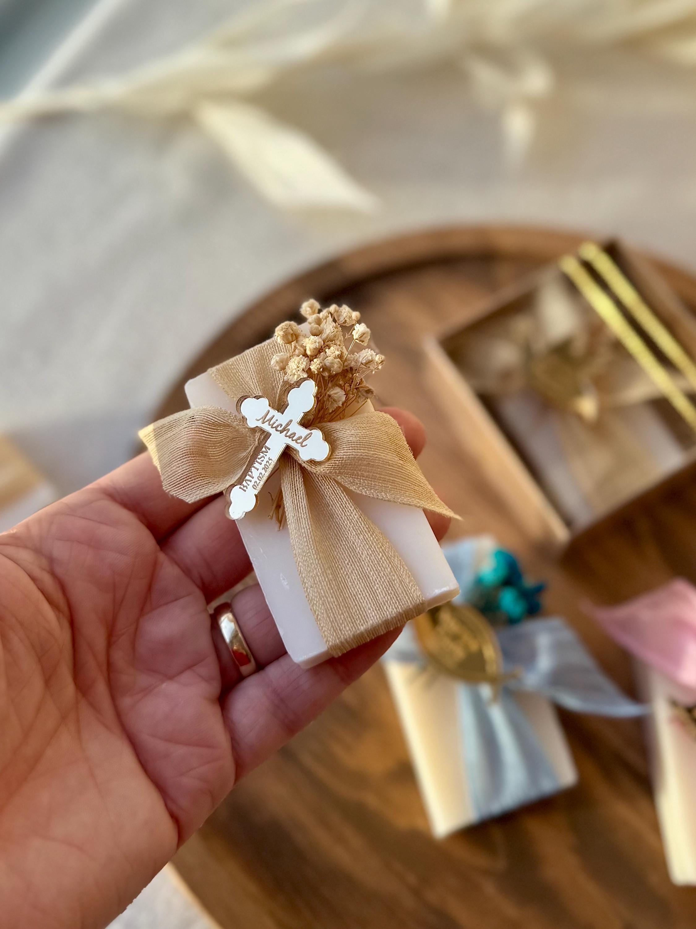 May include: A small white soap bar wrapped in a beige ribbon with a wooden cross charm that says &#39;Michael&#39; and &#39;Baptism&#39; on it. The cross charm is decorated with dried flowers.